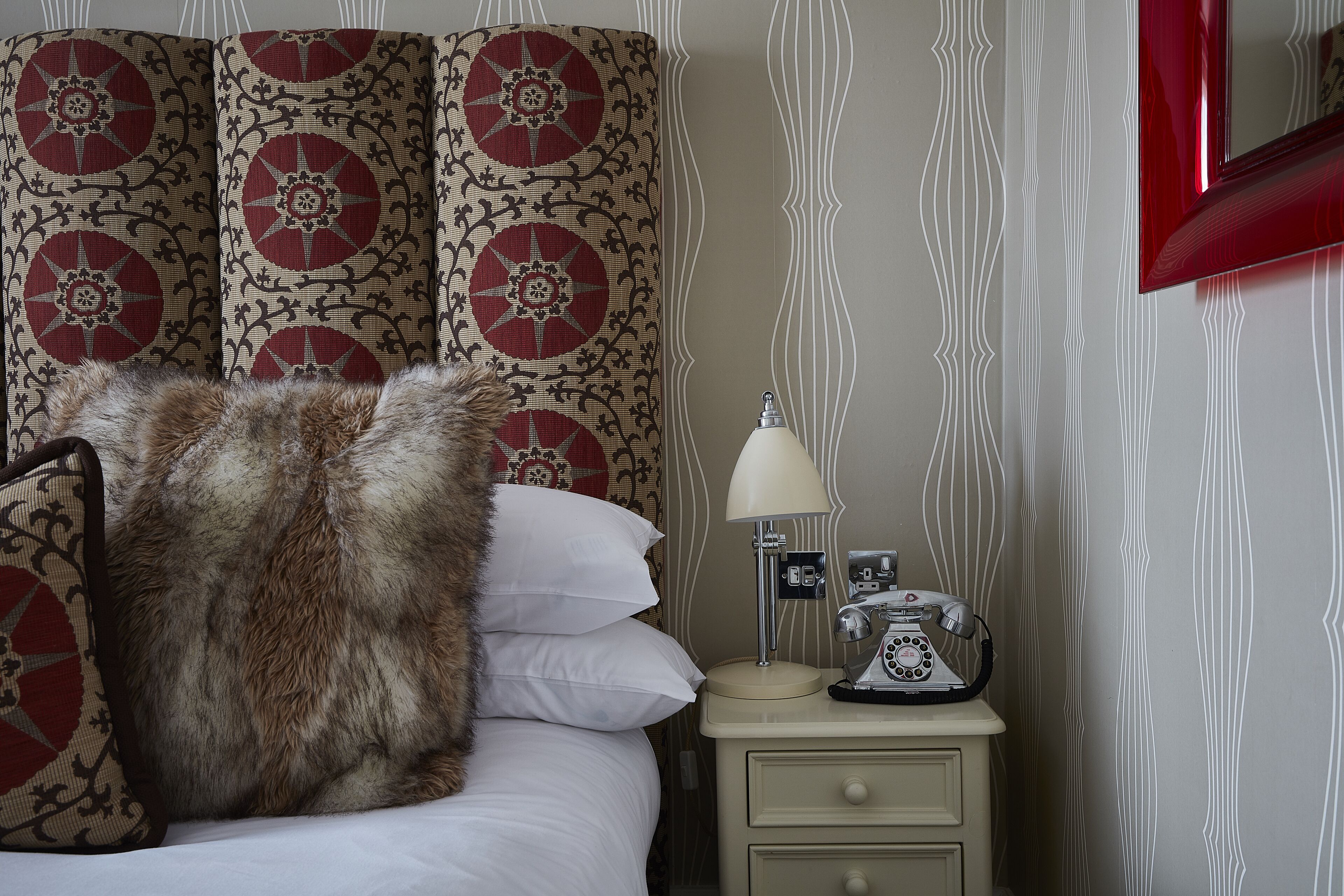 A neatly made bed with a large fur throw, a vintage telephone, and a bedside lamp on a nightstand.