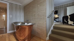 A bathroom with a copper bathtub, wooden flooring, and patterned walls.