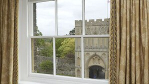 A window with a view of a castle-like structure with stone walls and a gate.
