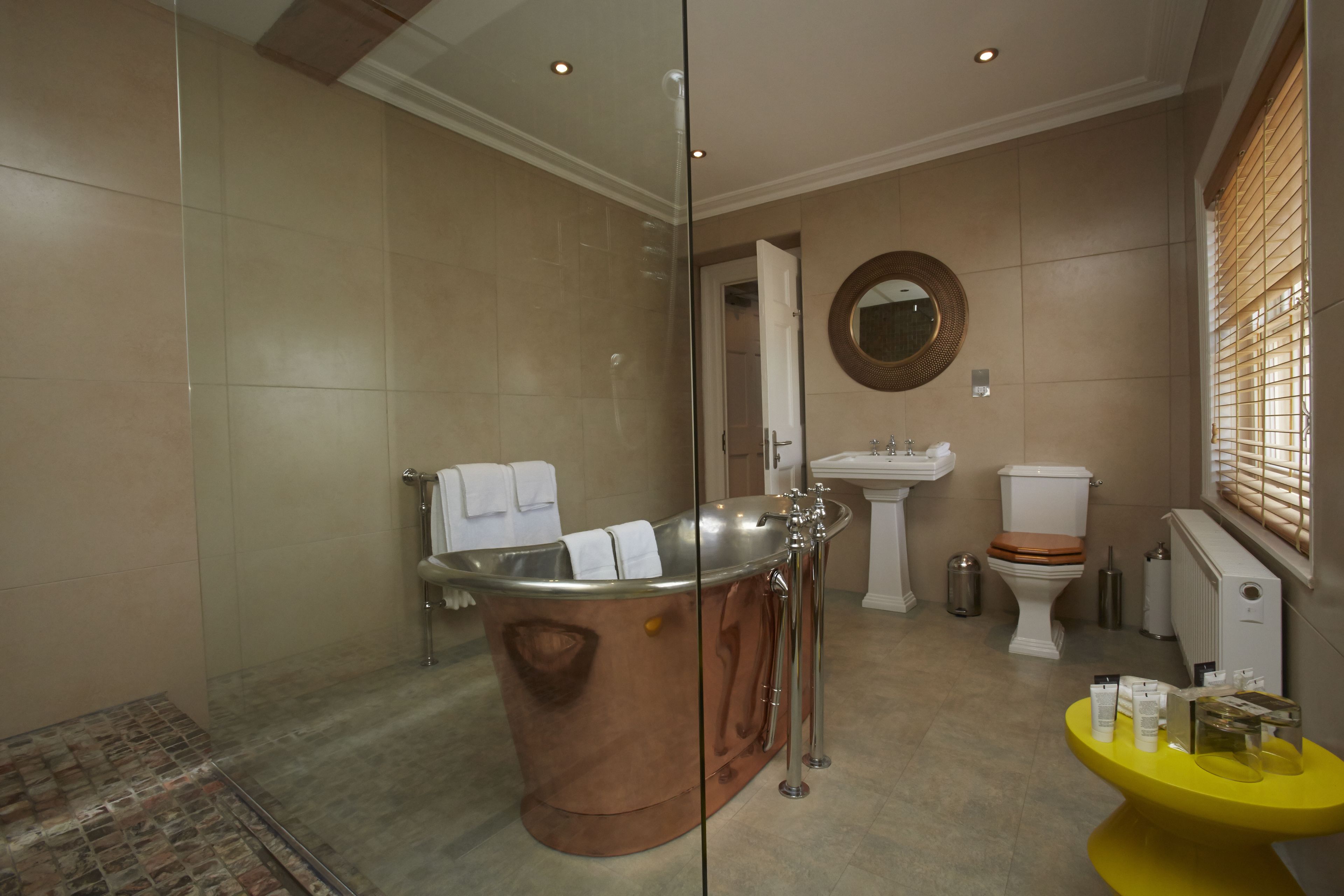 A modern bathroom with a copper bathtub, a pedestal sink, and a toilet.
