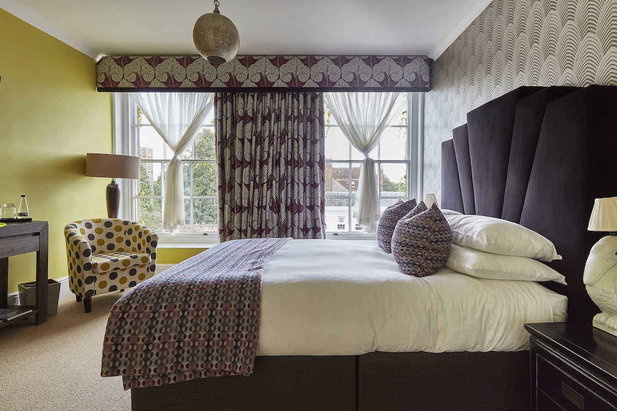 A bedroom with a large bed, a chair, a desk, and a window with curtains.