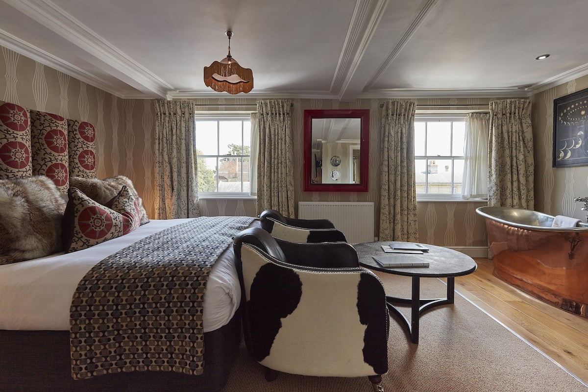 A hotel room with a bed, a round table, a chair, a bathtub, and a mirror.