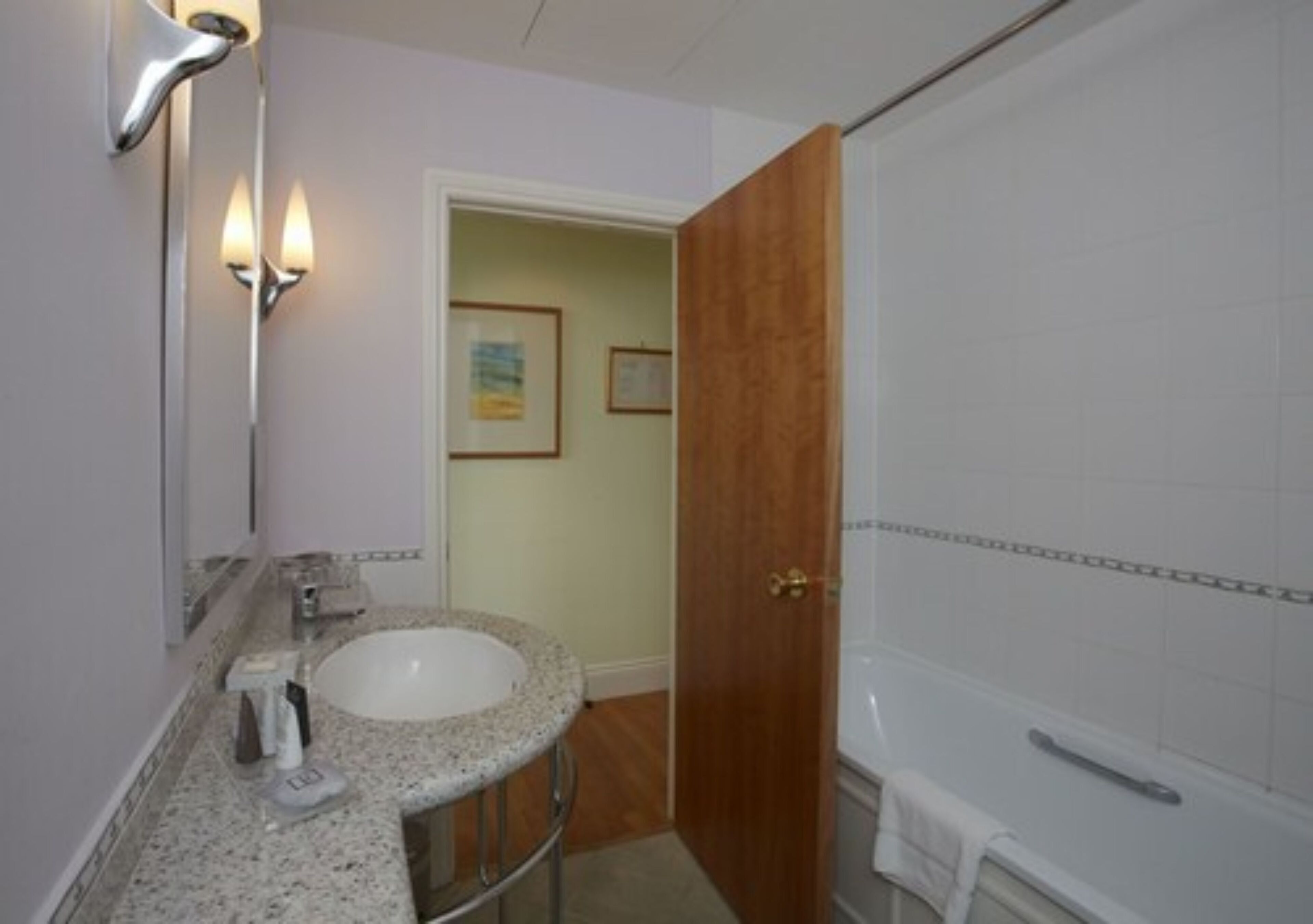 A bathroom with a granite countertop sink, a mirror, a shower, and a wooden door.