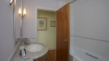 A bathroom with a granite countertop sink, a mirror, a shower, and a wooden door.