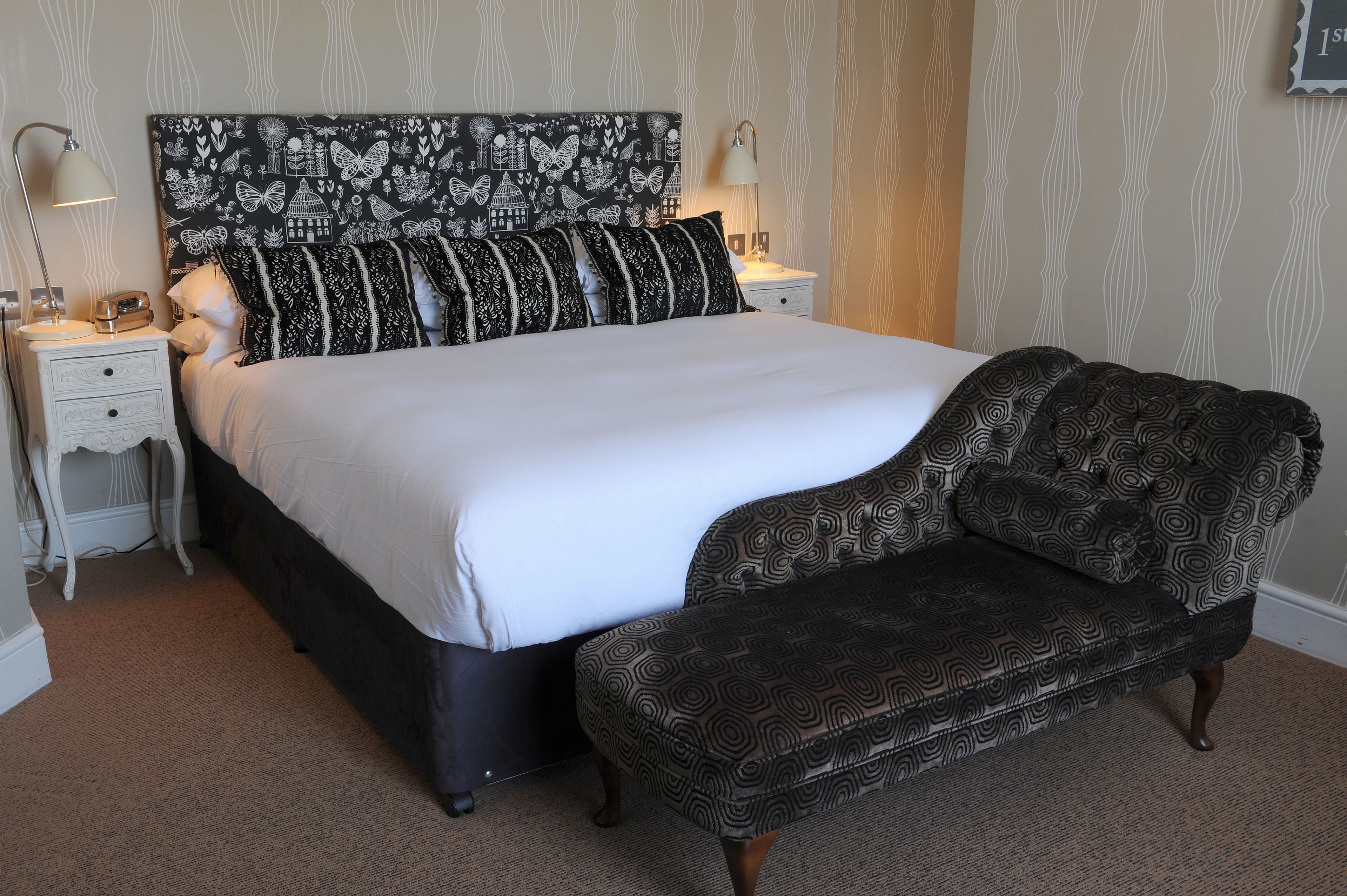 A bedroom with a large bed, two bedside tables, a nightstand, a patterned headboard, and a bench.