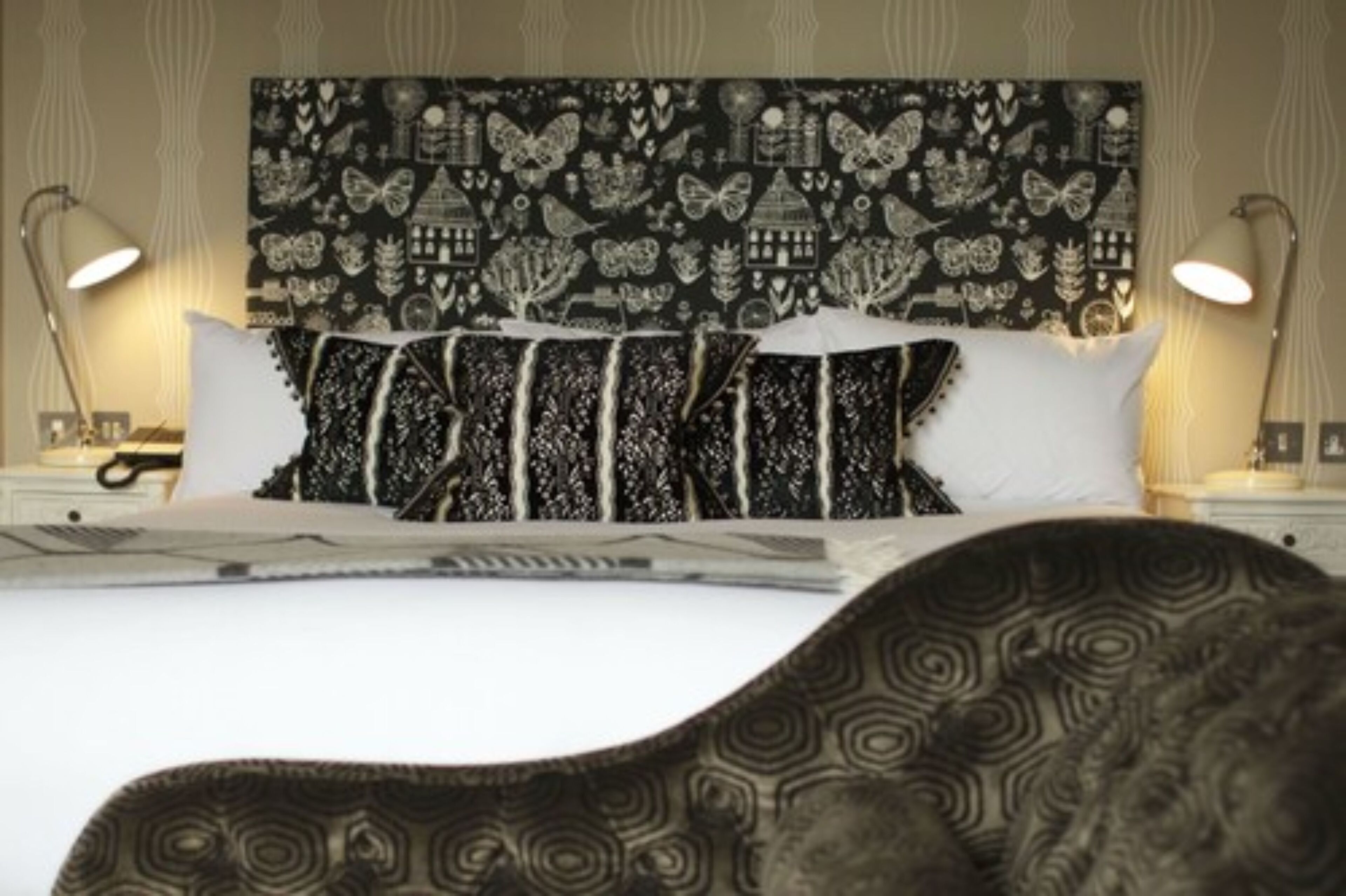 A neatly made bed with a patterned headboard, two bedside lamps, and a patterned throw pillow.