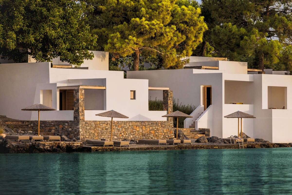 Un edificio moderno frente al mar, con piscina, paredes de piedra y mobiliario exterior.