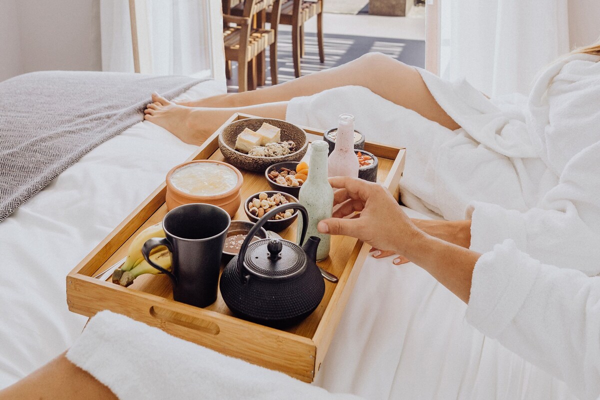 Un dormitorio con cama de madera, una bandeja con alimentos para el desayuno y vistas a una zona de piscina al aire libre.