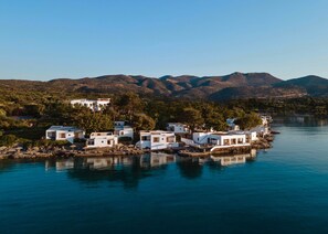 Un pueblo costero con edificios blancos, cielo azul despejado y montañas al fondo.
