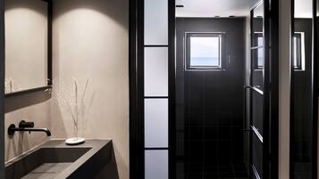 Un baño moderno con un espejo grande, un lavabo oscuro y vista al mar a través de una ventana.