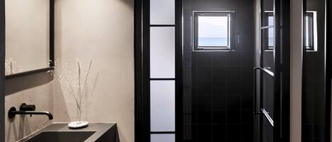 A modern bathroom with a large mirror, a dark sink, and a view of the sea through a window.