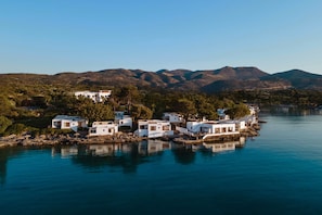 Un pueblo costero con edificios blancos, agua tranquila y montañas al fondo.