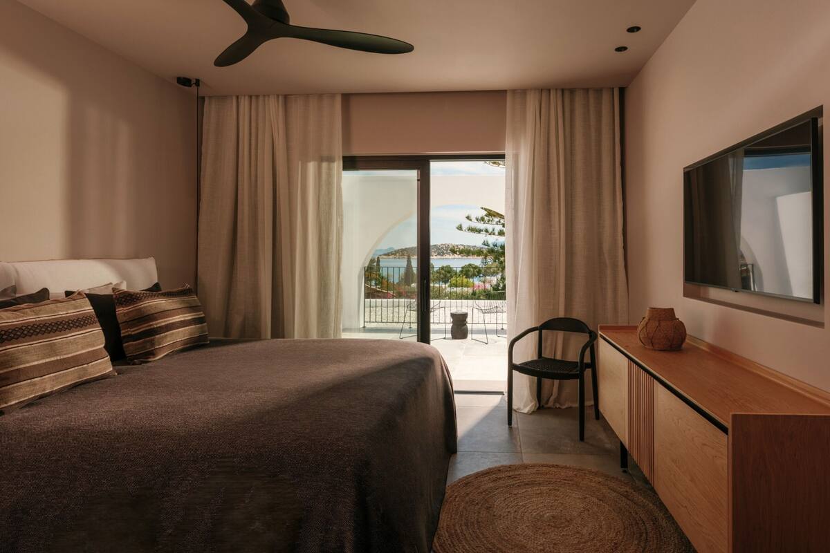 Un dormitorio con cama, escritorio, silla, televisor y balcón con vistas.
