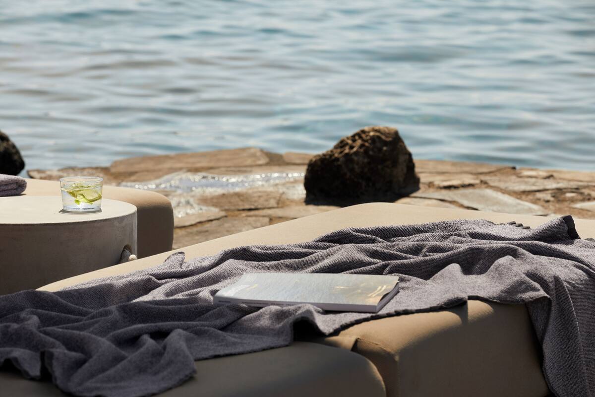 Un espacio de relax junto a la playa, con vista al mar, un vaso de agua y un libro sobre una silla.