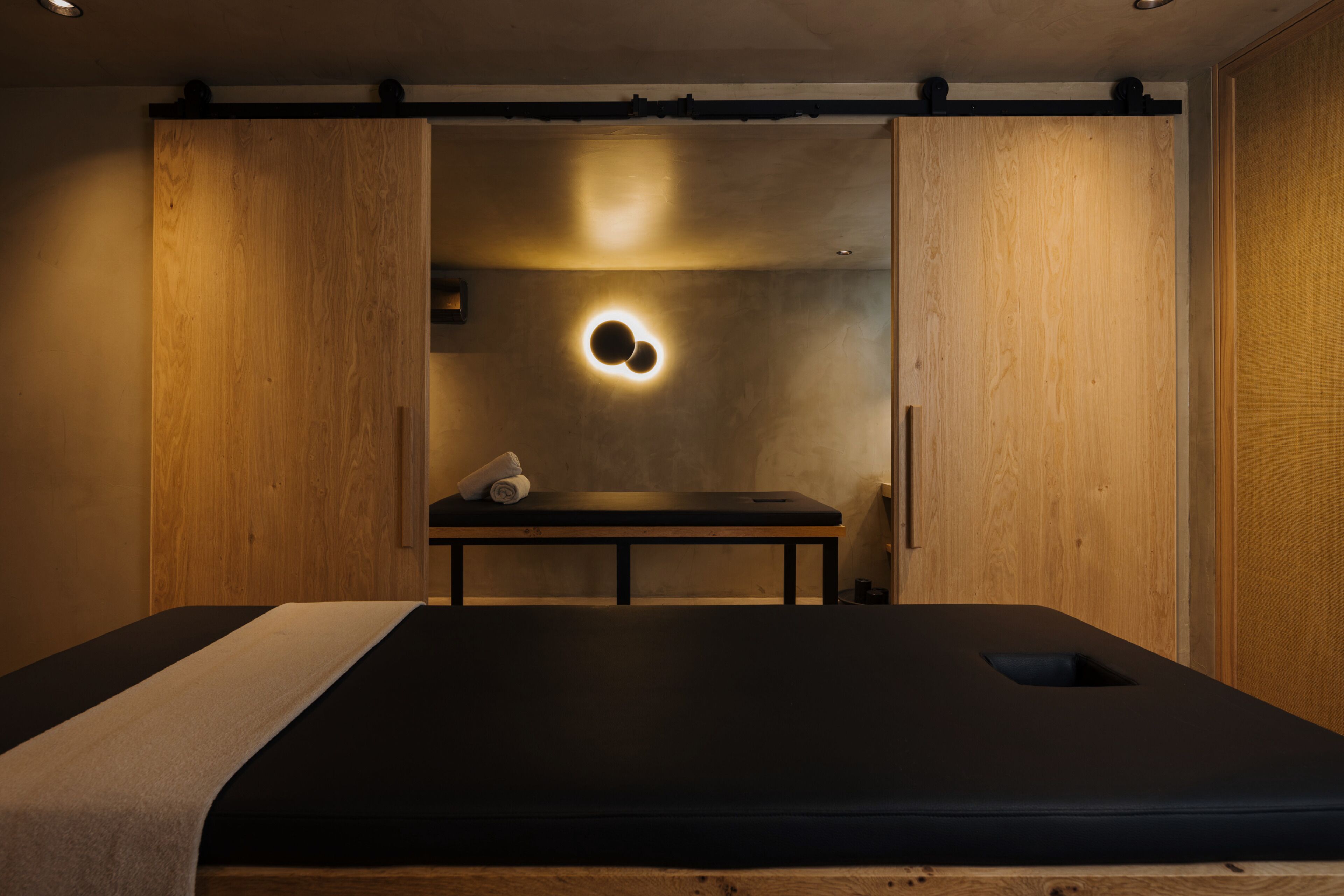 A room with a bed, a small table, and a wall-mounted light fixture.