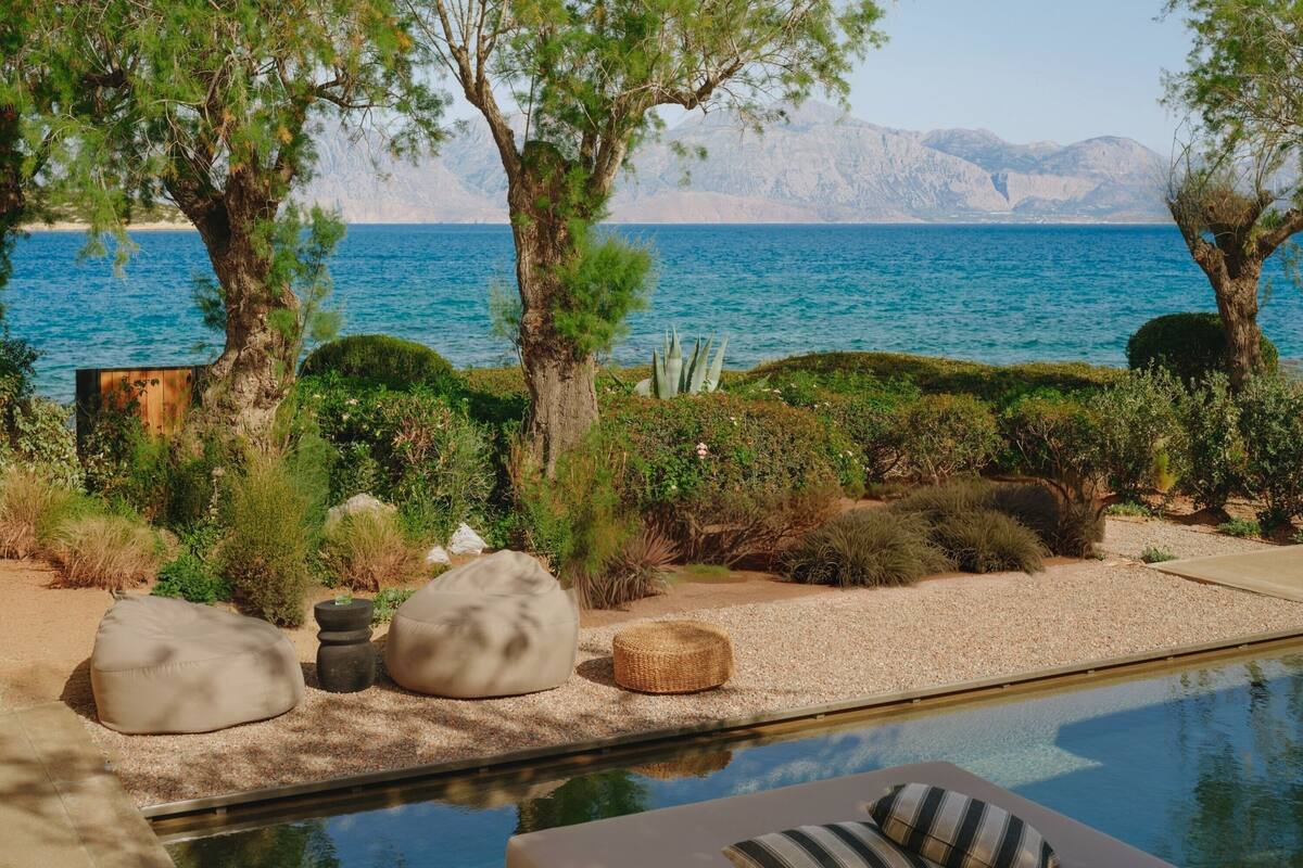 Zona junto a la piscina con vista al mar y las montañas, con una tumbona y una mesita.