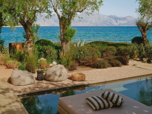 Zona junto a la piscina con vista al mar y las montañas, con una tumbona y una mesita.