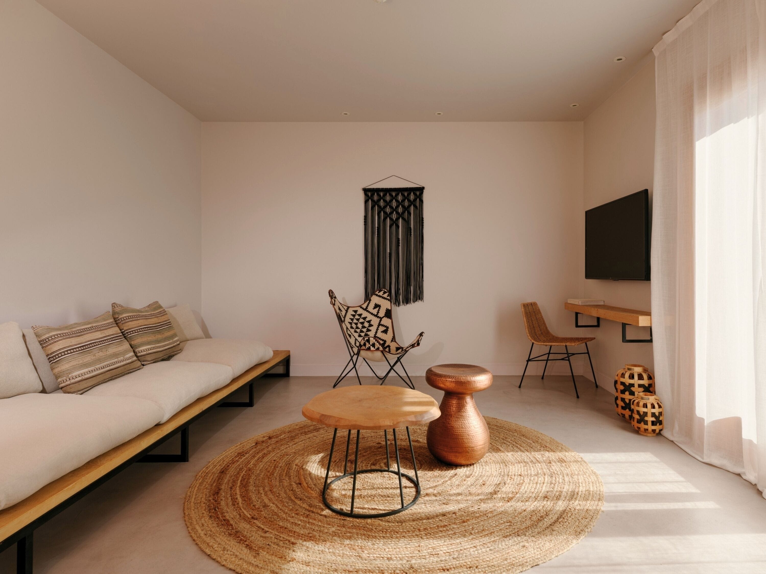 Un salon moderne comprenant un canapé, une table ronde en bois, un fauteuil, un téléviseur et des objets de décoration.
