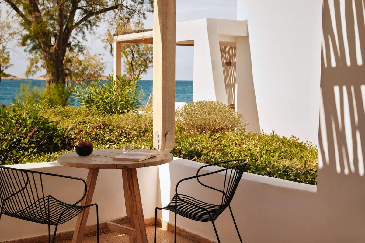 Una terraza con una mesa redonda y dos sillas, con vistas a una masa de agua y follaje exuberante.