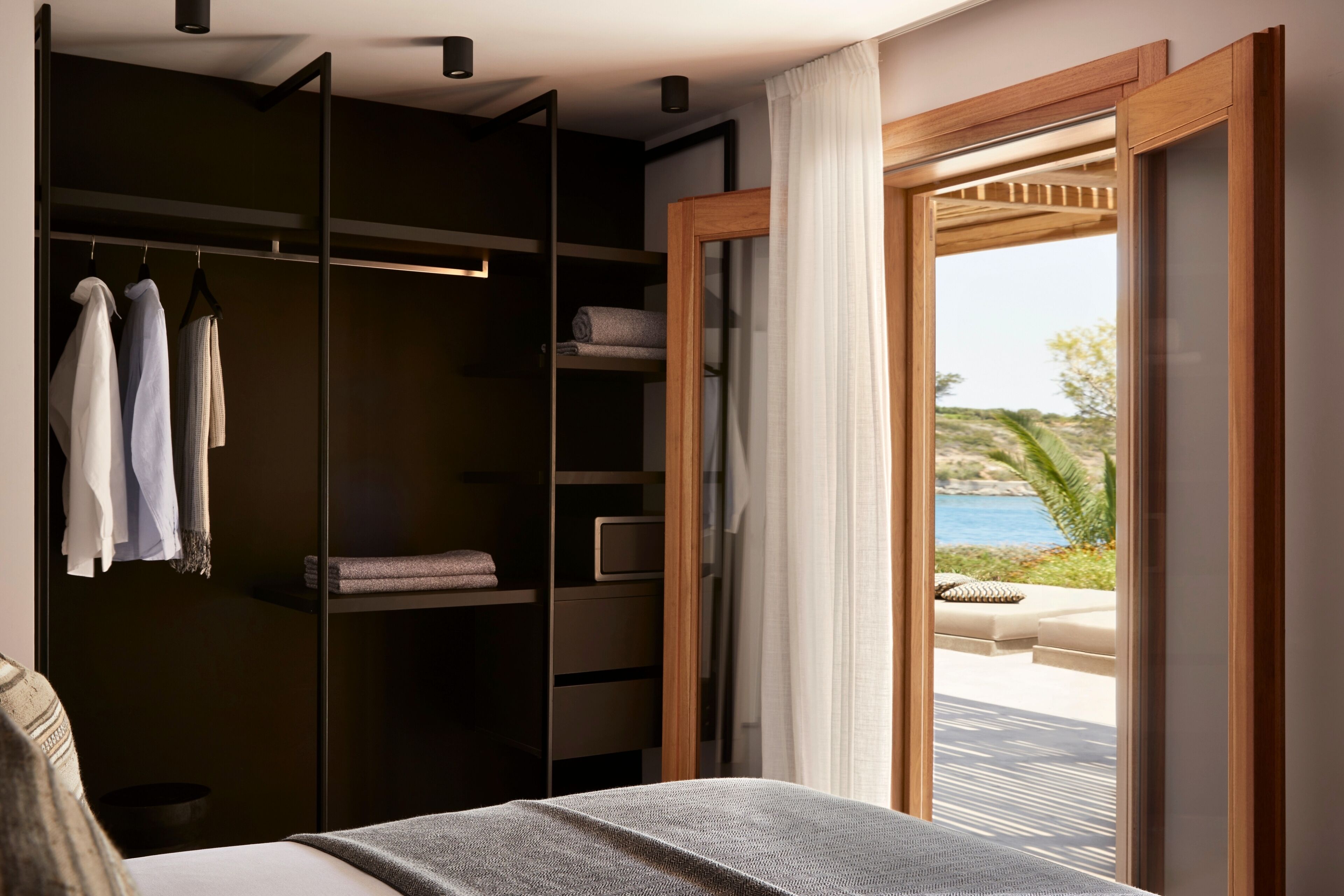 A bedroom with a bed, a wardrobe, and a view of a pool and beach.