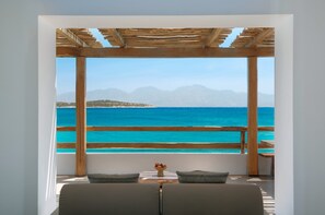 Une pièce offrant une vue sur la mer et les montagnes, avec une pergola en bois, un canapé et une petite table sur laquelle sont disposés des fruits.