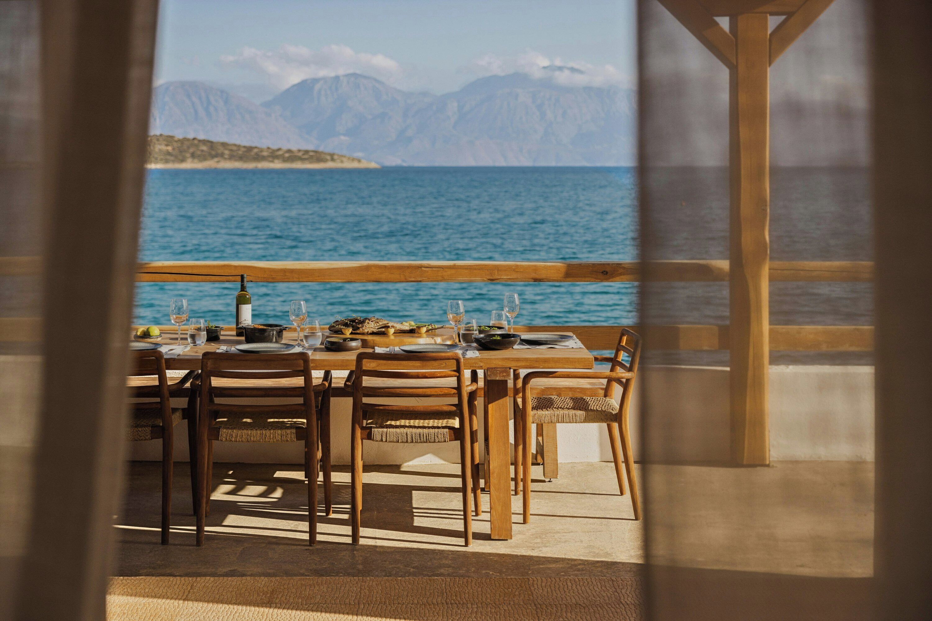 A wooden table set for dining with a view of the sea and mountains.