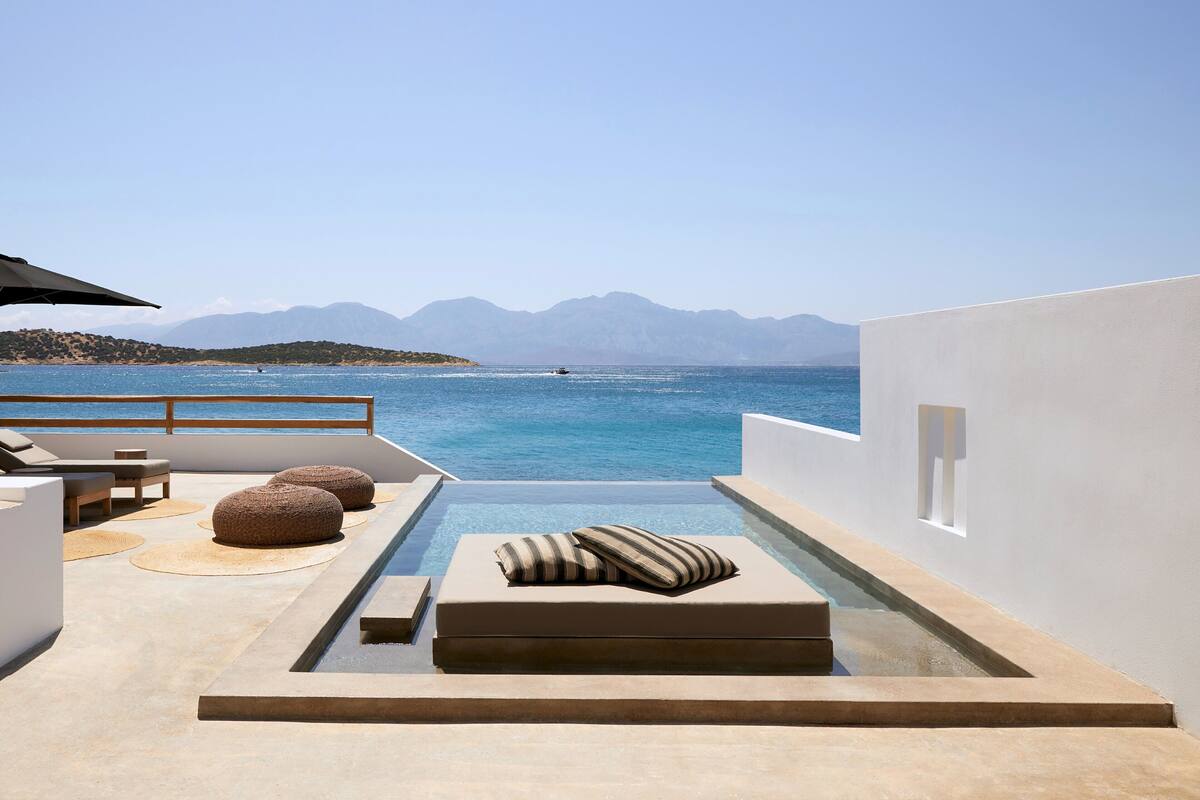 Zona junto a la piscina con vistas al mar y a las montañas, que incluye una tumbona, reposapiés y una mesita.