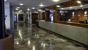 A hotel reception area with a marble floor, wooden reception desk, and clocks on the wall. - Hotel Fenix (Guadalajara)
