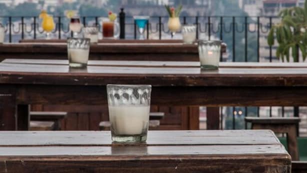 Outdoor wooden tables with glasses of milk and various drinks, overlooking a cityscape with buildings and a church spire. - Hotel Fenix (Guadalajara)