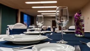 A dining table set with plates, cutlery, and wine glasses, with a vase of purple flowers in the background. - Hotel Fenix (Guadalajara)