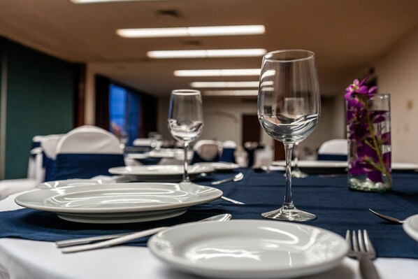 A dining table set with plates, cutlery, and wine glasses, with a vase of purple flowers in the background. - Hotel Fenix (Guadalajara)