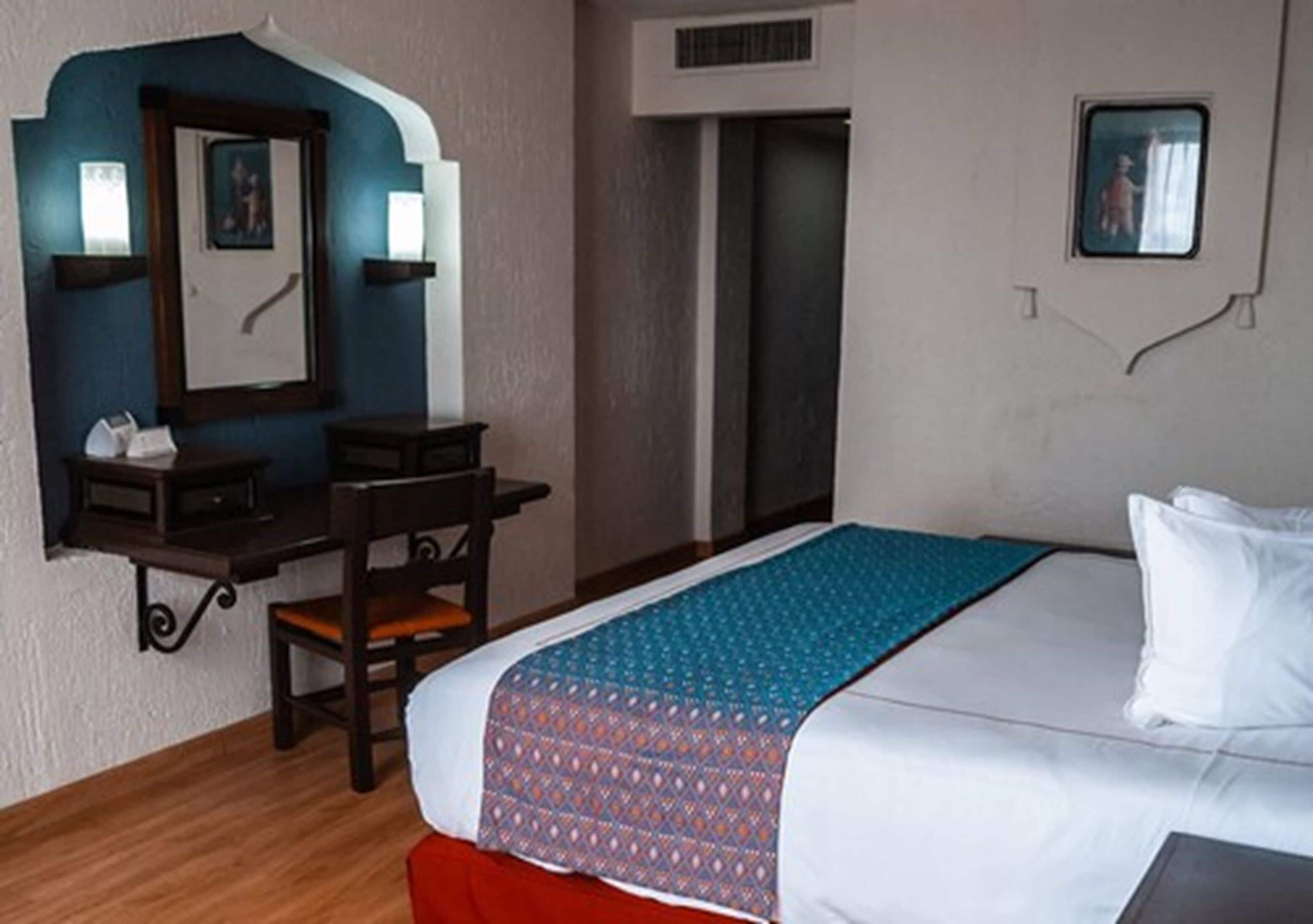 Habitació d'hotel amb un llit, escriptori, cadira, taula petita i finestra.