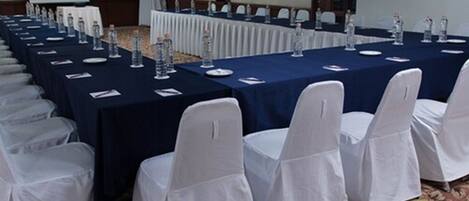 A conference room with long tables, white chairs, and water bottles.