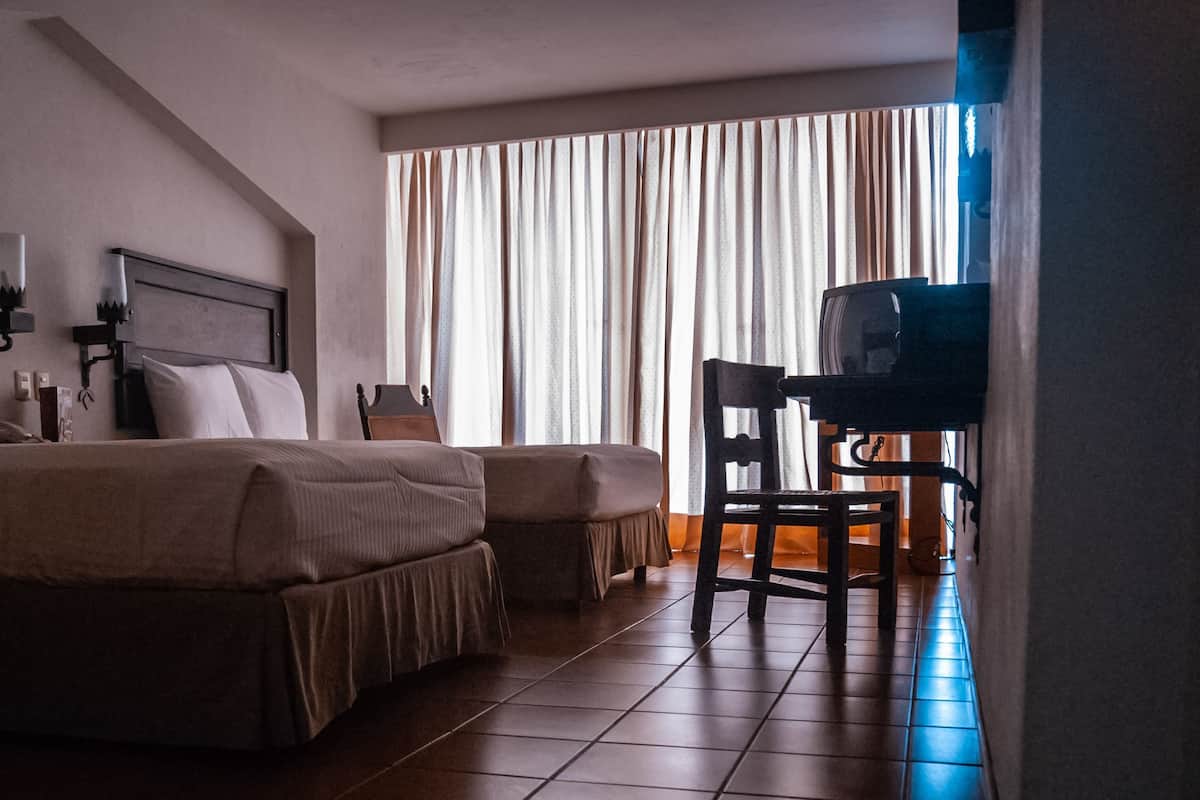 Una habitación de hotel con cama, escritorio, silla, televisor y cortinas.