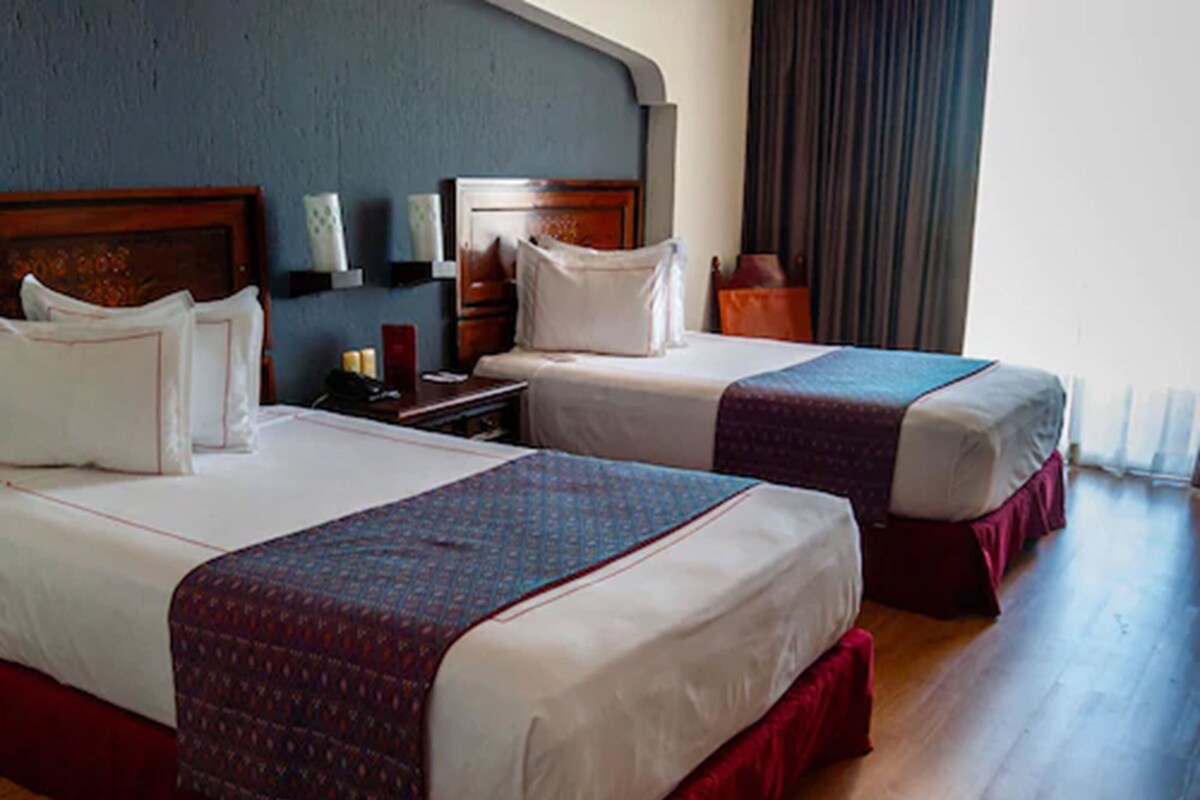 Two single beds with headboards, a bedside table, a lamp, and a window with curtains.