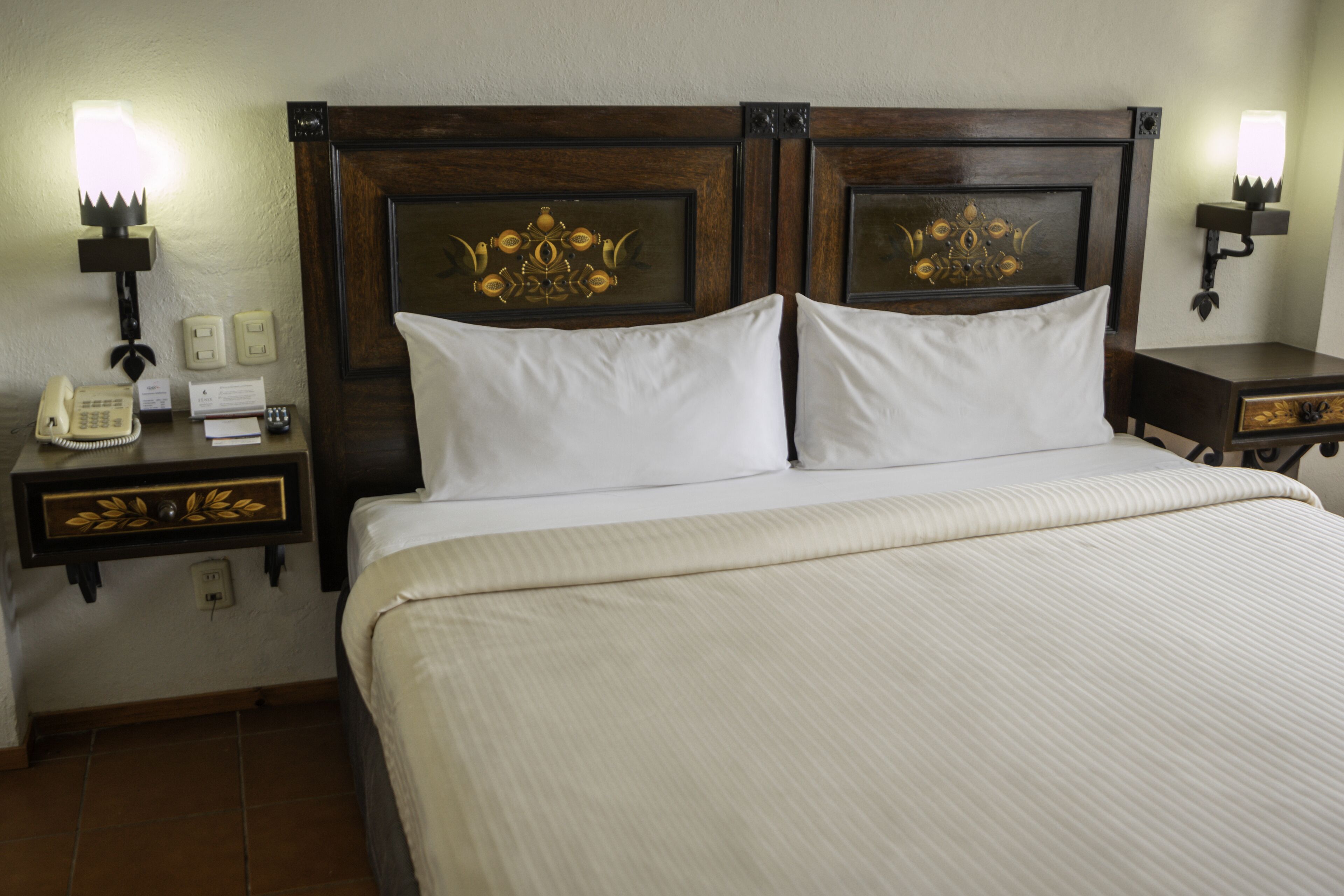 A hotel room with a large bed, two bedside tables, a nightstand, a telephone, and wall-mounted lamps.