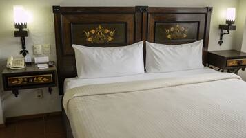 A hotel room with a large bed, two bedside tables, a nightstand, a telephone, and wall-mounted lamps.