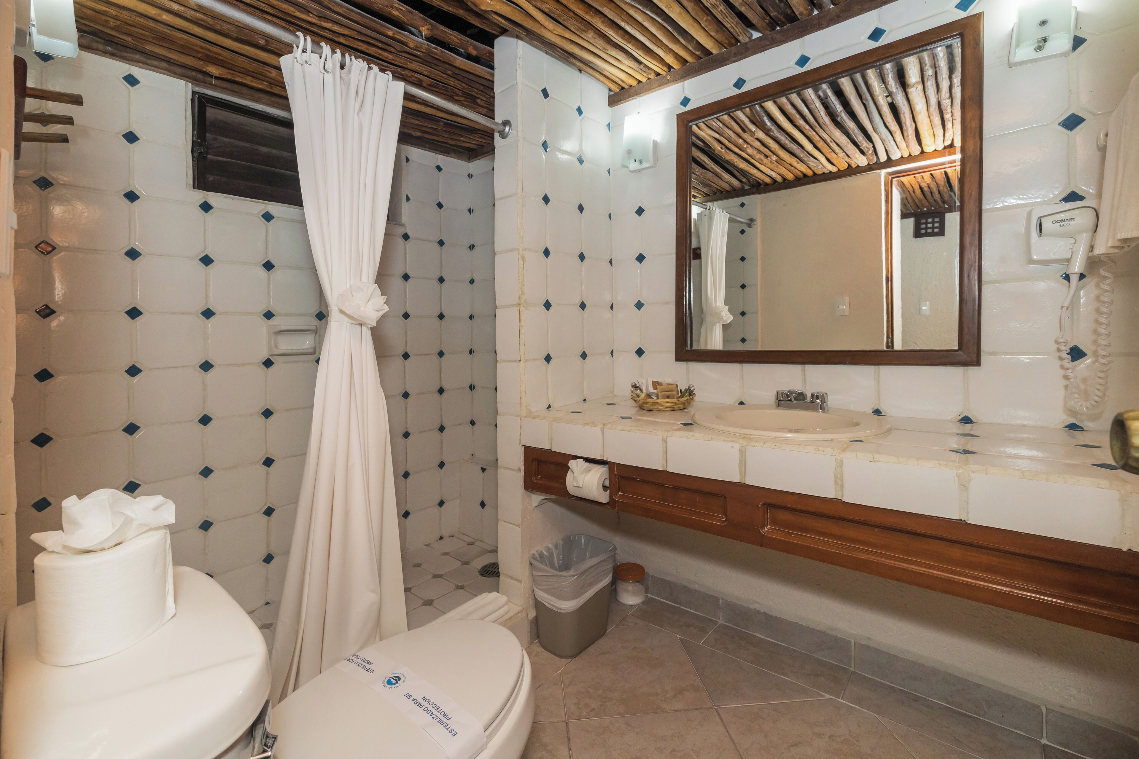 A bathroom with a toilet, a shower with a curtain, a sink, a mirror, and a trash bin.