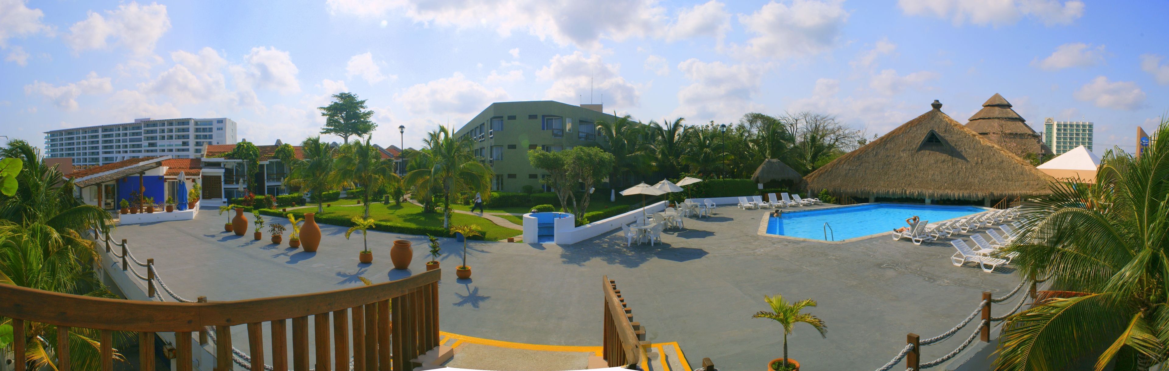 A resort with a swimming pool, lounge chairs, and a thatched-roof building.