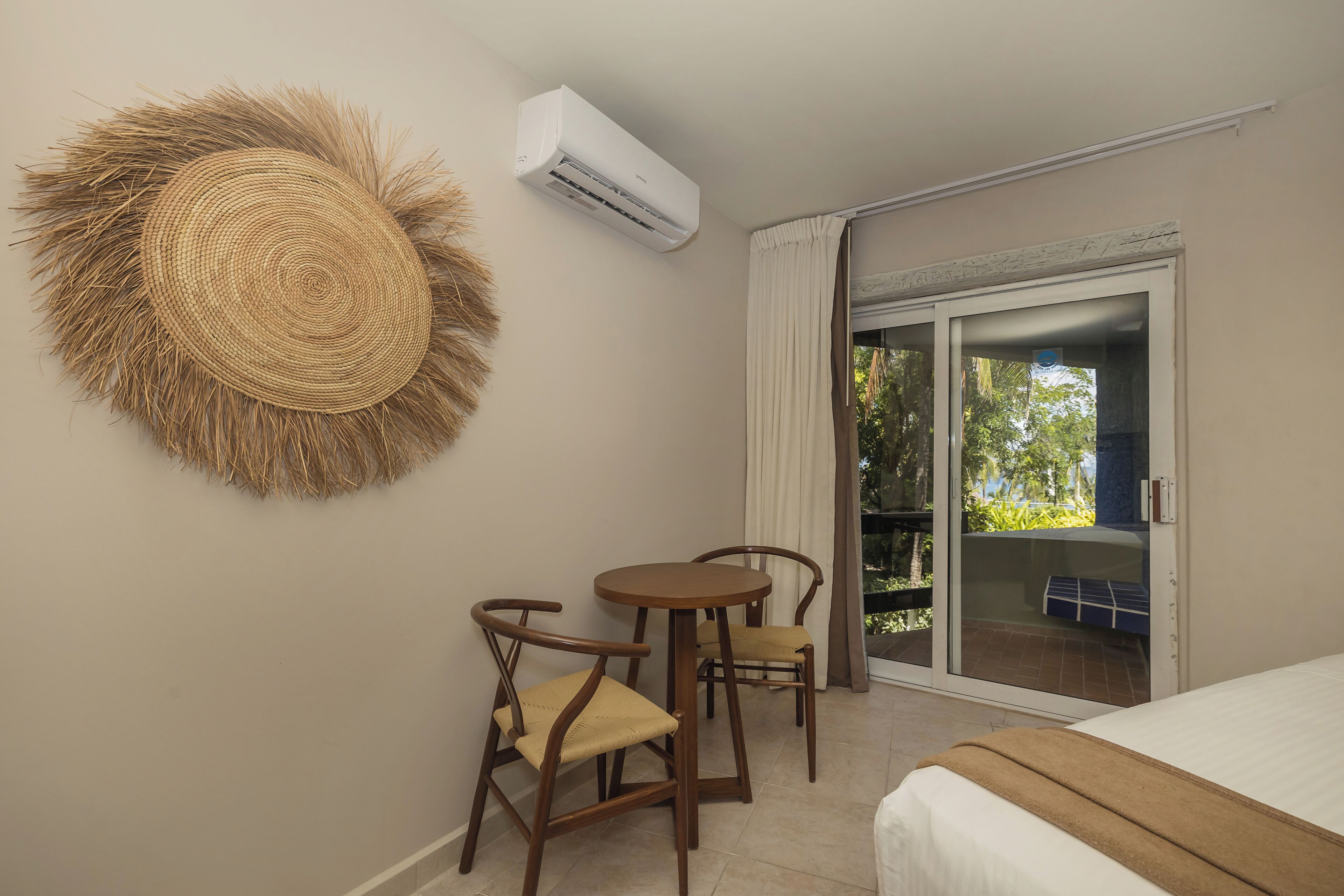 Una habitación con una cama, un tapiz redondo tejido en la pared, una pequeña mesa con sillas y una puerta corredera de cristal que da a un espacio exterior.