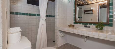 A bathroom with a toilet, shower, sink, and mirror.