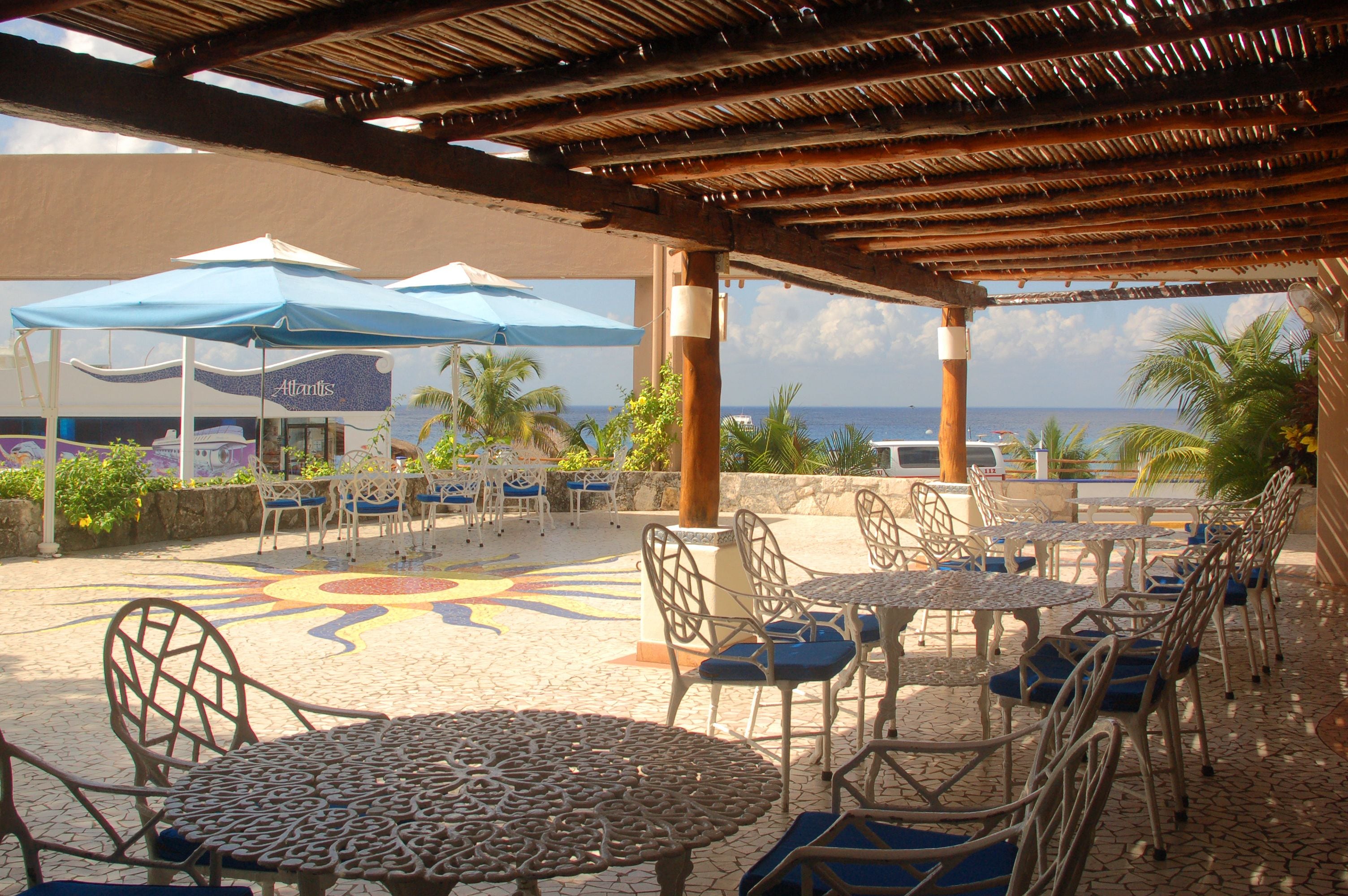 An outdoor patio area with tables and chairs, umbrellas, and a view of the ocean.