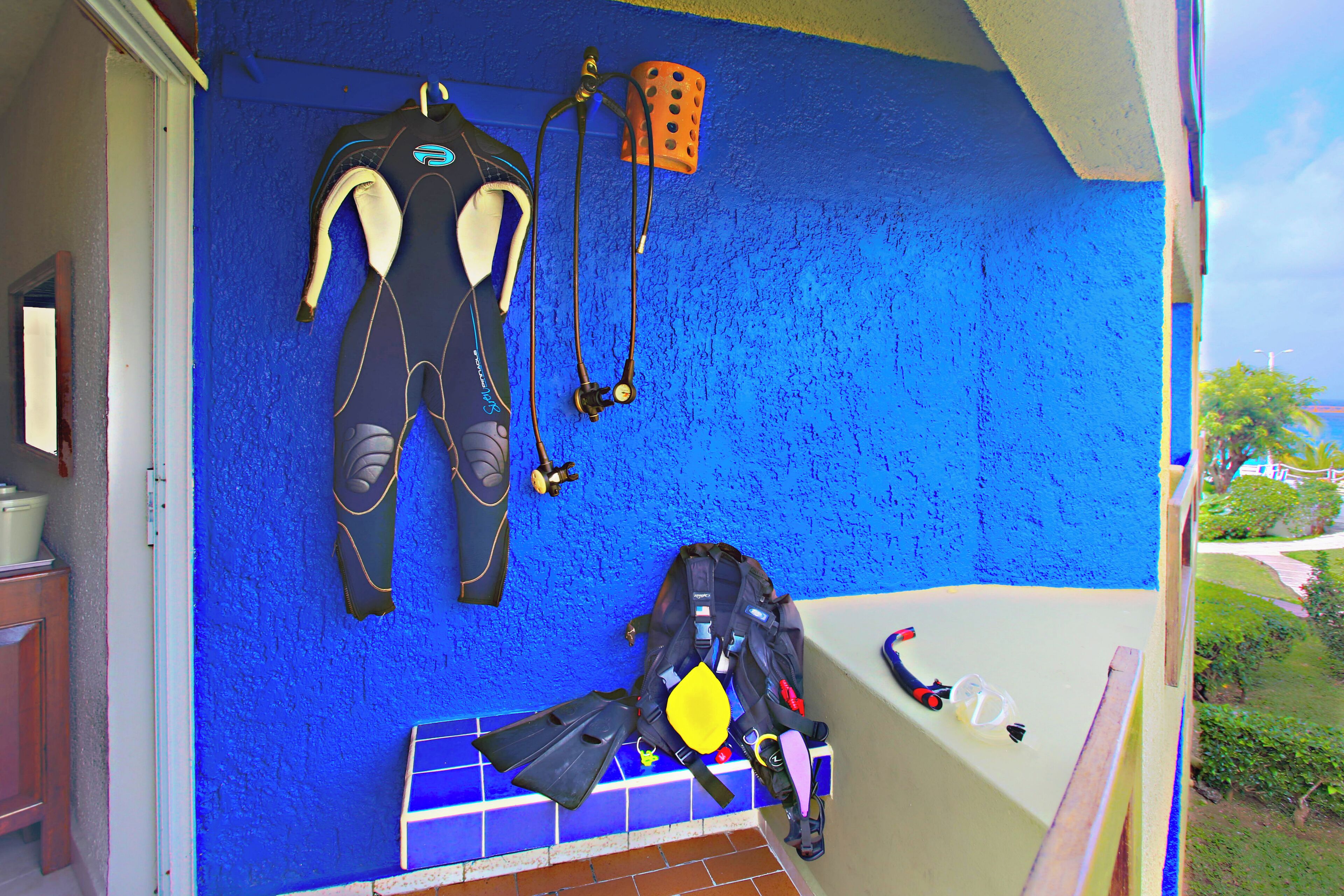 Quarto com parede azul texturizada, uma banheira e equipamento de mergulho, incluindo nadadeiras, fato de mergulho e máscara.