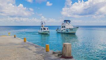 Two boats docked at a pier with clear blue water and a partly cloudy sky.