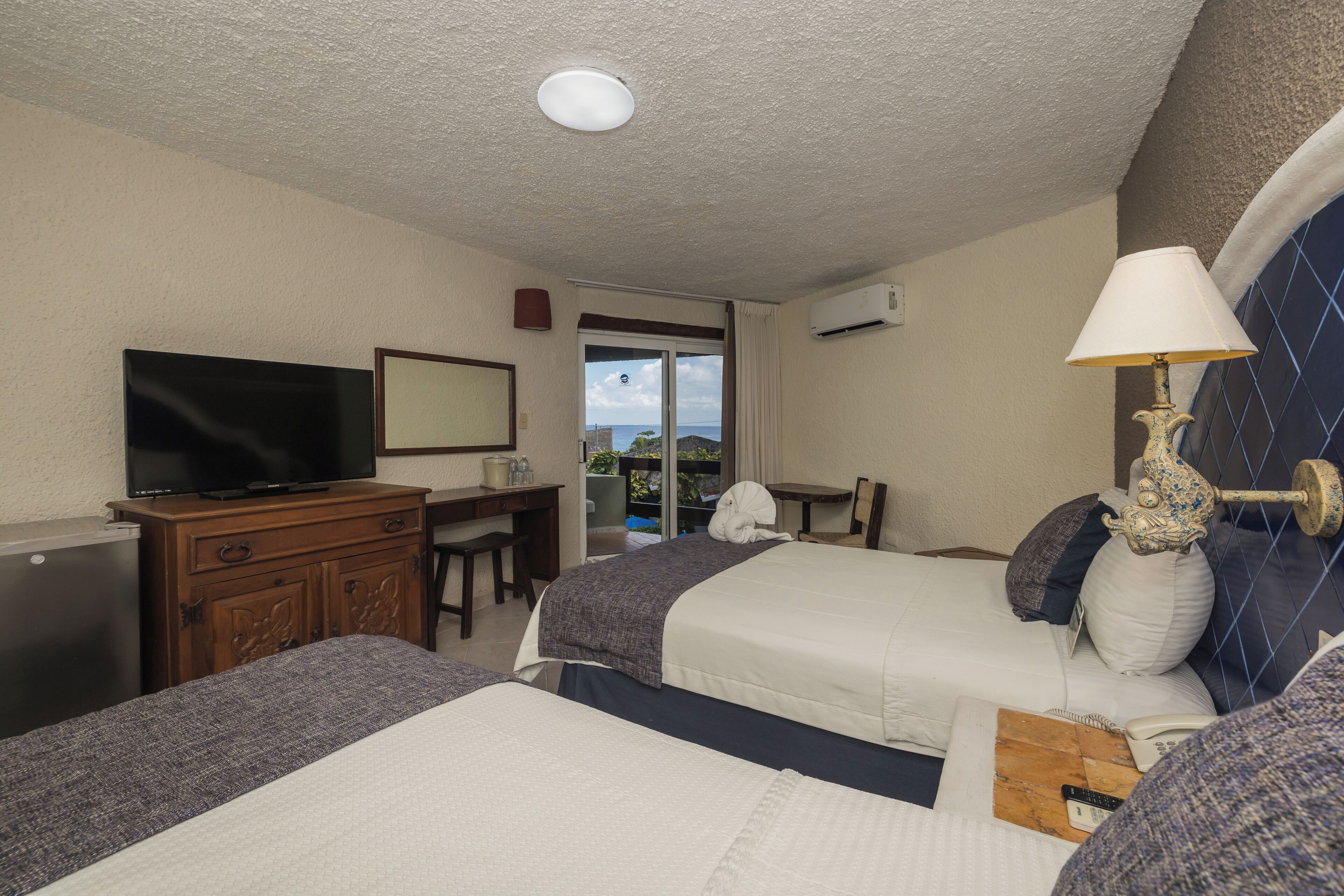 A hotel room with two beds, a TV, a desk, and a view of the outdoors.
