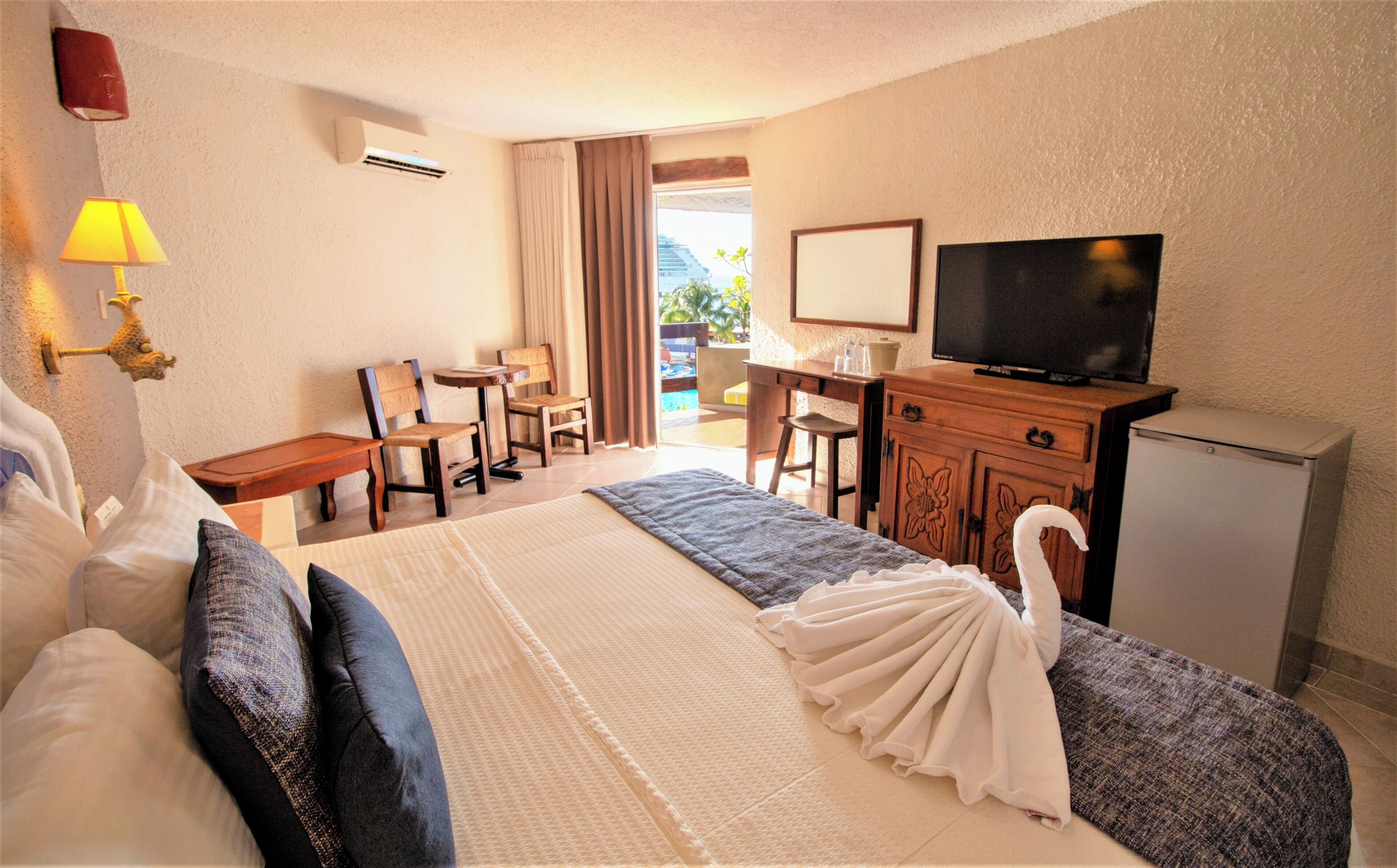 A hotel room with a bed, a desk, a television, and a view of the outdoors.