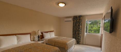 A hotel room with two beds, a nightstand, a lamp, an air conditioning unit, a window with curtains, and a flat-screen TV mounted on the wall.