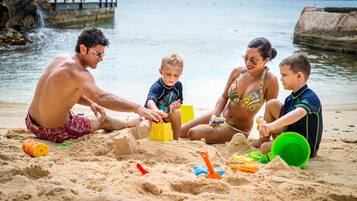 A family of four playing with sand on a beach with a rocky shoreline and a pier in the background.