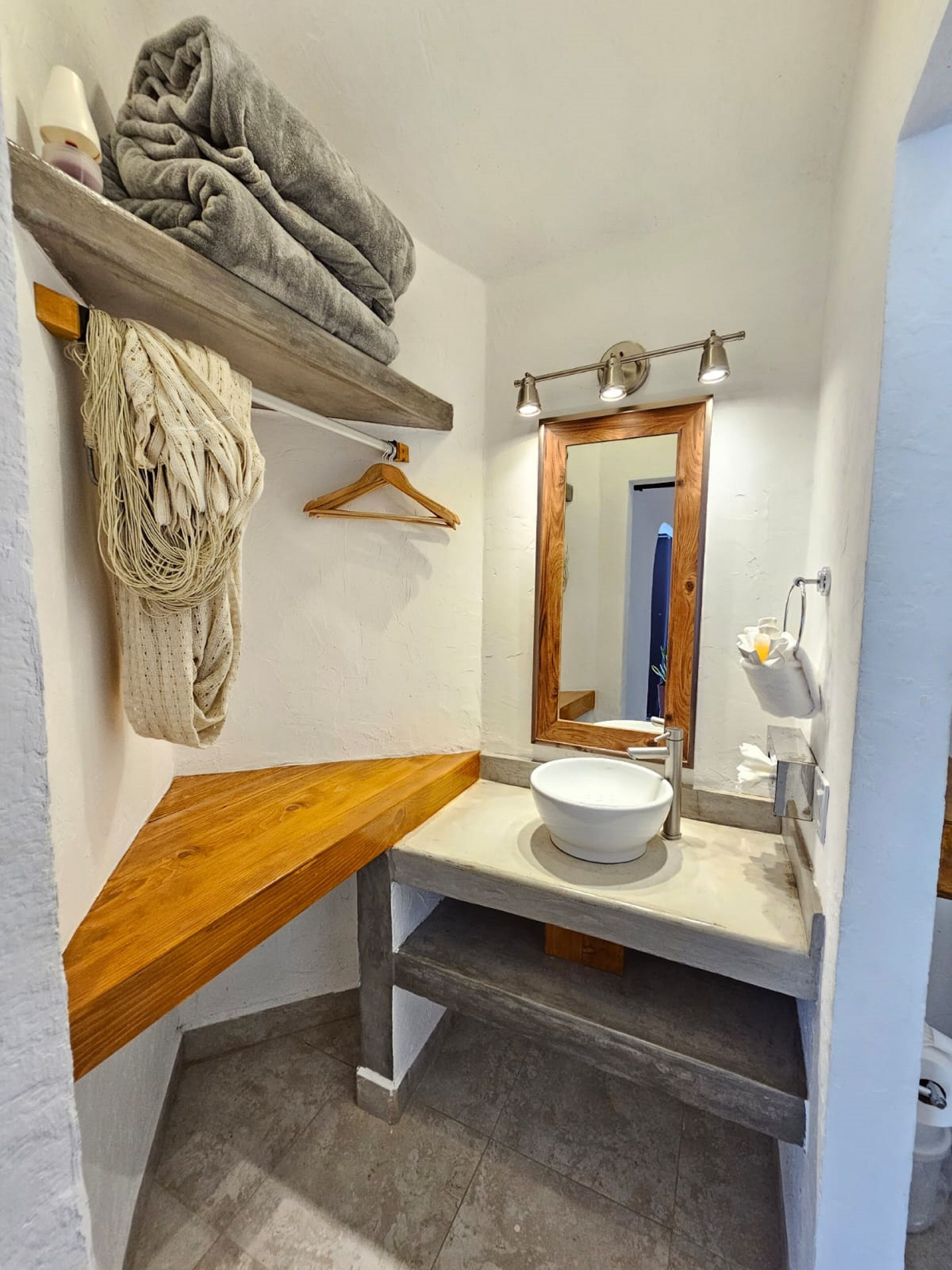 Ein Badezimmer mit einem Holzbadezimmermöbel, einem weißen Waschbecken, einem Spiegel mit Beleuchtung und einem Handtuchhalter.