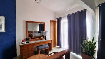 A room with a wooden desk, a mirror, a chair, a potted plant, and a window with curtains.
